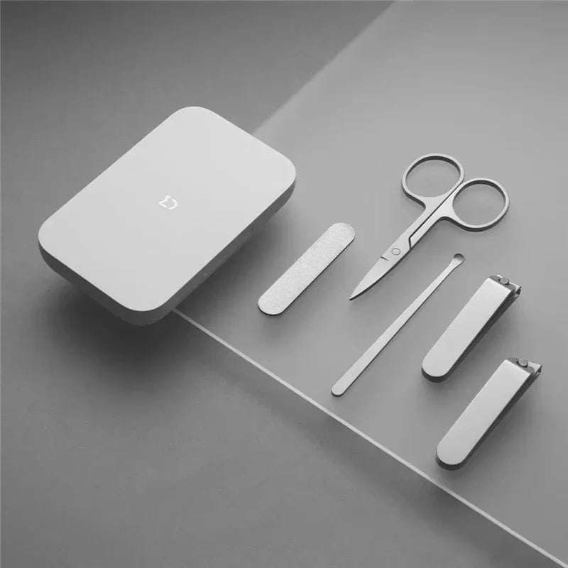 Set of grooming tools including a white square container, scissors, and nail clippers on a gray surface.